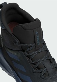 Bota de senderismo negra y azul marino con un upper texturizado, collar acolchado y ojales reforzados, con acentos azules y suela duradera.