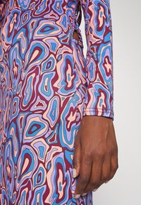 Sukienka z długim rękawem, zdobiona kolorowym, abstrakcyjnym wzorem w odcieniach fioletu, niebieskiego i różowego. Materiał jest gładki z delikatnym stretch'em i starannie wykonanym przeszyciem.