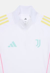 Vit träningsjacka med dragkedja i kragen. Har gula och rosa accenter samt ljusblå Adidas- och Juventus-logotyper på bröstet.