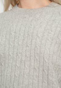 Világosszürke kötött pulóver, amely kábelmintás kötést, bordázott nyakrészt és puha textúrát kínál, meleg és kényelmes viseletre tervezve.