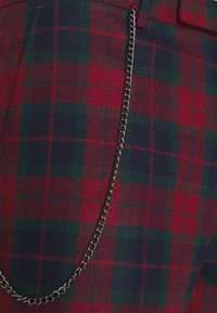 Rood en groen geruite stof met een wolachtige textuur, met een zilveren metalen ketting bevestigd voor detail.