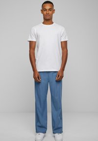 Hvid bomulds T-shirt parret med lyseblå denimbukser, begge i afslappet pasform, og afsluttet med hvide sneakers. Ensartet farveskema.