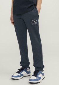 Pantalones de chándal azul marino con un logo blanco en el muslo izquierdo, hechos de una tela suave, con un ajuste relajado y puños elásticos.