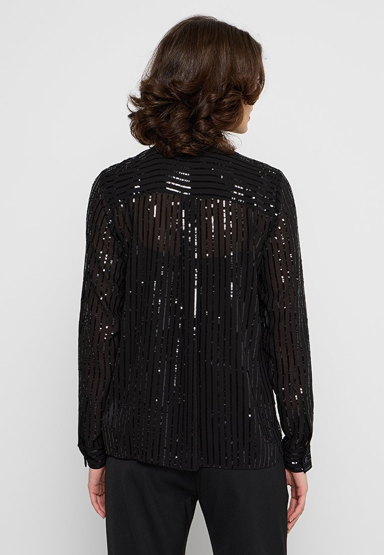 Zwarte doorzichtige blouse met verticale paillettenstrepen, lange mouwen en een plooi aan de achterkant. Gladde textuur, casual pasvorm en ronde halslijn.