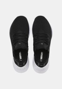 Mustat urheilujalkineet, joissa on teksturoitu yläosa, litteät nauhat ja valkoiset pohjat. Sisältää brändättyjä yksityiskohtia kengänkielessä ja kantapäässä.