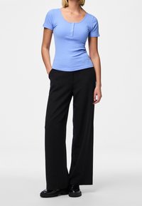 Svetle modré žebrované tričko s krátkým rukávem a kulatým výstřihem, doplněné o tříknoflíkovou légou, v kombinaci s černými širokými kalhotami a černými botami.