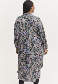 Sukienka w kwiaty na ciemno brązowym tle, z niebieskimi i zielonymi wzorami kwiatowymi, długimi rękawami i luźnym krojem. Widok z tyłu.