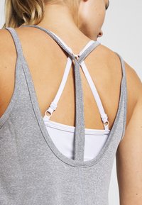 Top gris sin mangas con diseño de espalda deportiva y tirantes blancos, confeccionado en un tejido texturizado. Detalles destacados en la parte trasera incluyen herrajes ajustables.