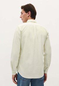Camicia a maniche lunghe a righe verde chiaro con colletto button-down, dettaglio sullo yoke posteriore e polsini con un bottone, abbinata a jeans blu.