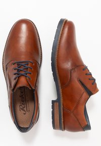 Zapatos de vestir de cuero marrón con un acabado suave, puntera redonda, cordones azul marino y acentos texturizados marrones contrastantes en la suela.
