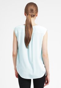 Blusa senza maniche di un blu chiaro con vestibilità rilassata, texture liscia, orlo arrotondato e dettaglio di piega discreto sul retro.