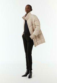 Beżowa puchowa kurtka ze wzorem pikowania z wysokim kołnierzem, ściągaczami na rękawach i zapięciem na zamek. W połączeniu z czarnymi spodniami i botkami za kostkę. Gładka tekstura.