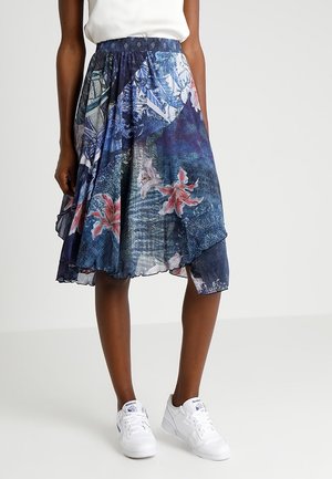 Flydende blå nederdel med lyserøde blomster- og abstrakte mønstre, båret med hvide sneakers og en hvid ærmeløs top.