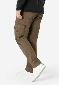 Cargo-Hosen aus olivgrünem Baumwollmaterial mit mehreren Taschen, enger zulaufenden Beinen und sichtbaren Nähdetails, kombiniert mit weißen Sneakers.