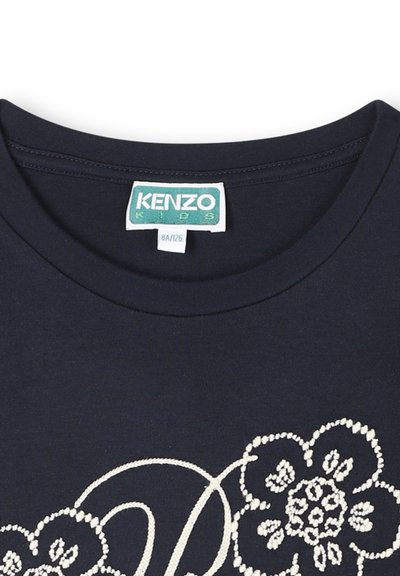 T-shirt en coton bleu marine avec un col rond, présentant une broderie florale blanche et la lettre "D" en style cursif. Étiquette KENZO Kids visible.