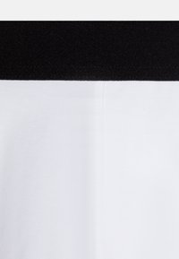 Svart elastisk midje i toppen, hvit bomullsstoff under med en glatt tekstur, som har et enkelt og rent design.