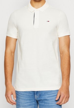 Chemise polo blanche à manches courtes, avec un col à boutons et un petit logo sur la poitrine gauche. Fabriquée en tissu de coton lisse.