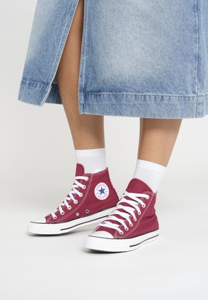 Ben iført hvide sokker og røde høje Converse-sneakers med hvide snørebånd, kombineret med en lyseblå denimnederdel med en frontslids.