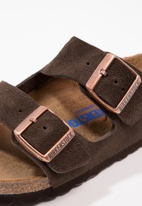 Sandale en suede marron avec deux brides réglables et boucles en bronze, semelle en liège moulé et semelle texturée pour une meilleure adhérence.