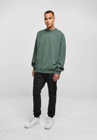 Zeleni oversized dukserica s rebrastim manžetama i donjim rubom, u kombinaciji s crnim tapered sportskim hlačama i bijelim tenisicama. Jednostavna, ležerna odjeća.