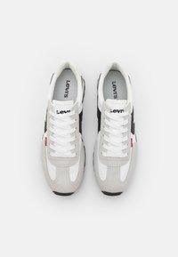 Graue, weiße und schwarze Sneaker aus einer Mischung aus Wildleder und Stoff. Sie verfügen über auffällige Schnürsenkel, ein Logo auf der Zunge und eine strukturierte Sohle.