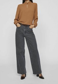 Brun långärmad blus med nyckelhålskrage och volangärmar, tillsammans med högmidjade, vida mörka jeans och svarta klackskor.