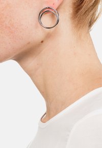 Orecchini in metallo argento con un design a doppio cerchio, caratterizzati da due anelli intrecciati, texture liscia e finitura lucida.