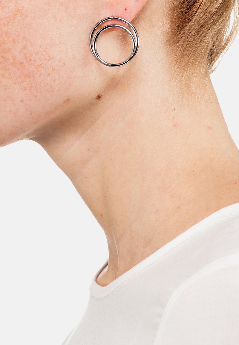 Orecchini in metallo argento con un design a doppio cerchio, caratterizzati da due anelli intrecciati, texture liscia e finitura lucida.