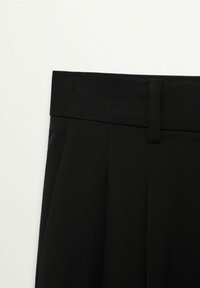 Pantalon noir taille haute avec passants pour ceinture et plis avant sur un fond clair uni, montrant le détail de la zone supérieure de la taille.