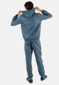 Chándal ligero y azul con puños y cintura elásticos. La chaqueta con capucha presenta una textura suave; los pantalones tienen un corte recto y puños en los tobillos.