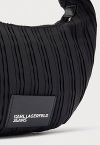 Czarna plisowana torba na ramię wykonana z tkaniny o teksturowanej powierzchni. Posiada zamek błyskawiczny oraz etykietę z logo z czarnej skóry.