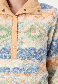 Fleece pullover met pastel swirl patronen, lichtbruine drukknoopkraag, zachte textuur en een klein logo op de borst.