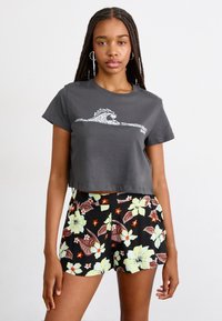 Gray cropped t-shirt with white wave graphic, paired with black shorts featuring floral pattern in green, brown, and orange hues.