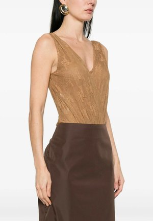 Donna che indossa un top smanicato color beige in pizzo con scollatura a V profonda e gonna a vita alta di colore marrone scuro, accessoriata con grandi orecchini rotondi dorati.