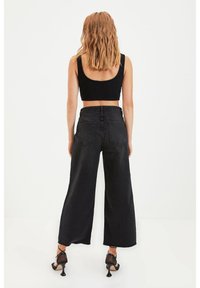 Jean large noir en denim, avec une taille haute, deux poches arrière et des ourlets effilochés. Associé à un crop top noir et des talons.