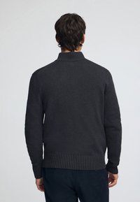 Dunkelgrauer Strickpullover mit hohem Kragen, gerippten Bündchen und Taillenbund. Er zeichnet sich durch eine glatte Textur und ein figurbetontes Design aus.