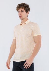 Polo de color naranja claro hecho de una tela texturizada, con un pequeño logo, cuello clásico y mangas cortas con puños contrastantes.