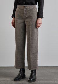 Brown checkered trousers made of woven fabric feature a straight fit, mid-rise waist, and a button closure. Paired with black ankle boots.