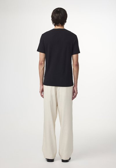Czarny t-shirt z krótkim rękawem w połączeniu z luźnymi beżowymi spodniami. T-shirt ma prosty fason i okrągły dekolt, wykonany z miękkiego materiału.
