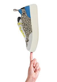 Sneaker z boku w cętkowanym wzorze lamparcim, szarym materiałem teksturowanym, niebieskimi akcentami, żółtymi sznurówkami i białą gumową podeszwą trzymany przez palec.