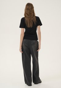 Sort tætsiddende t-shirt parret med løse, mørkegrå denimjeans. Outfittet har en jævn tekstur med minimale sømdetaljer og vide ben.
