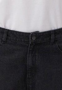 Czarne dżinsy o gładkiej fakturze, klasyczny pięciokieszeniowy krój oraz zapięcie na metalowy guzik. Pas wyposażony jest w szlufki na pasek.