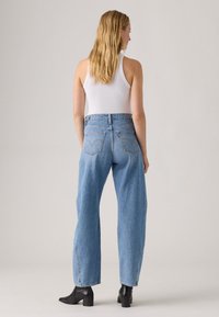 Blue denim jeans with a high waist and straight-leg design. Visible stitching and back pockets, paired with black ankle boots.
