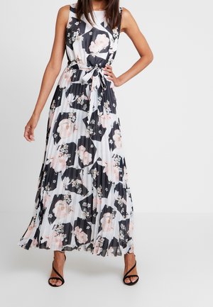 Maxi-jurk in donkere kleuren met een bloemenprint. Geplooide textuur, mouwloos ontwerp en een taille met strikdetail. Zwarte sandalen met bandjes.