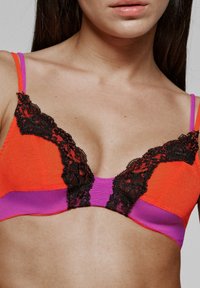 El bralette multicolor presenta una base naranja vibrante con acentos morados y un borde de encaje negro. El diseño enfatiza una forma de V profunda en la parte delantera.