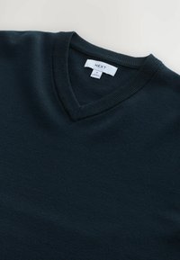Pulover bleumarin, cu mânecă lungă și decolteu în V, fabricat dintr-un material moale. Prezintă un guler și manșete ribbate. Eticheta indică brandul "NEXT" și mărimea "M."