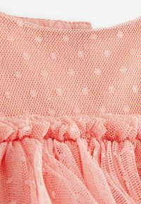 Robe rose clair avec un corsage en dentelle à pois texturée et une jupe en mesh à volants, mettant en valeur un tissu doux et transparent ainsi que des détails délicats.