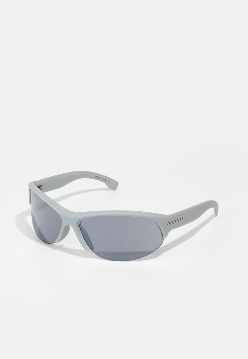 Gafas de sol grises con un diseño elegante y deportivo. Presentan lentes oscuros y un acabado mate en las monturas. Incluyen un sutil acento metálico en el lateral.
