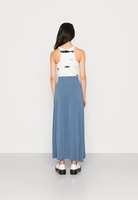Maxirok van zacht blauwe stof met een elastische tailleband, gecombineerd met een witte tanktop met een zwart tie-dye patroon. Robuuste witte schoenen.
