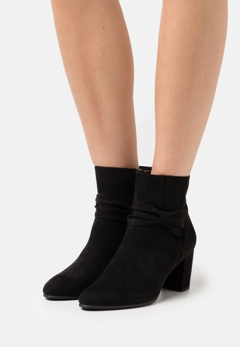 Bottines en suede noir avec un revers replié et un détail en nœud, dotées d'un bout pointu et d'un talon épais. Texture lisse dans l'ensemble.
